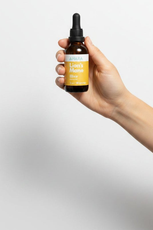 A hand holding the AHARA Lion's Mane Elixir against a soft grey background
